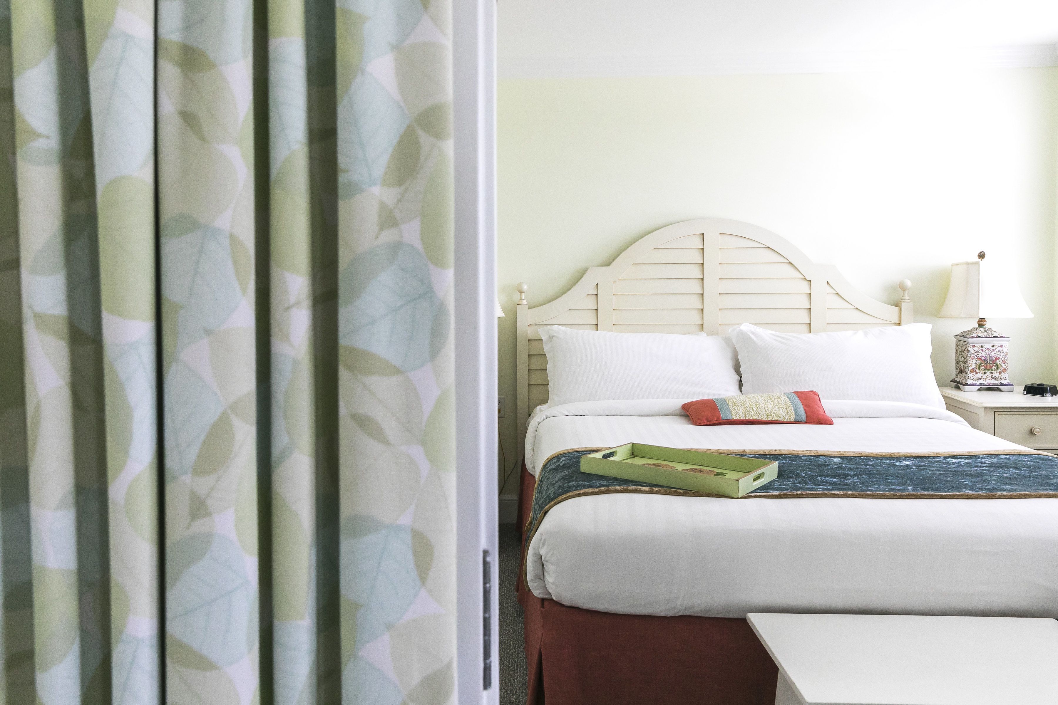 Een netjes opgemaakt bed met witte lakens en een groene dienblad, een houten hoofdbord en een nachtkastje met een lamp.