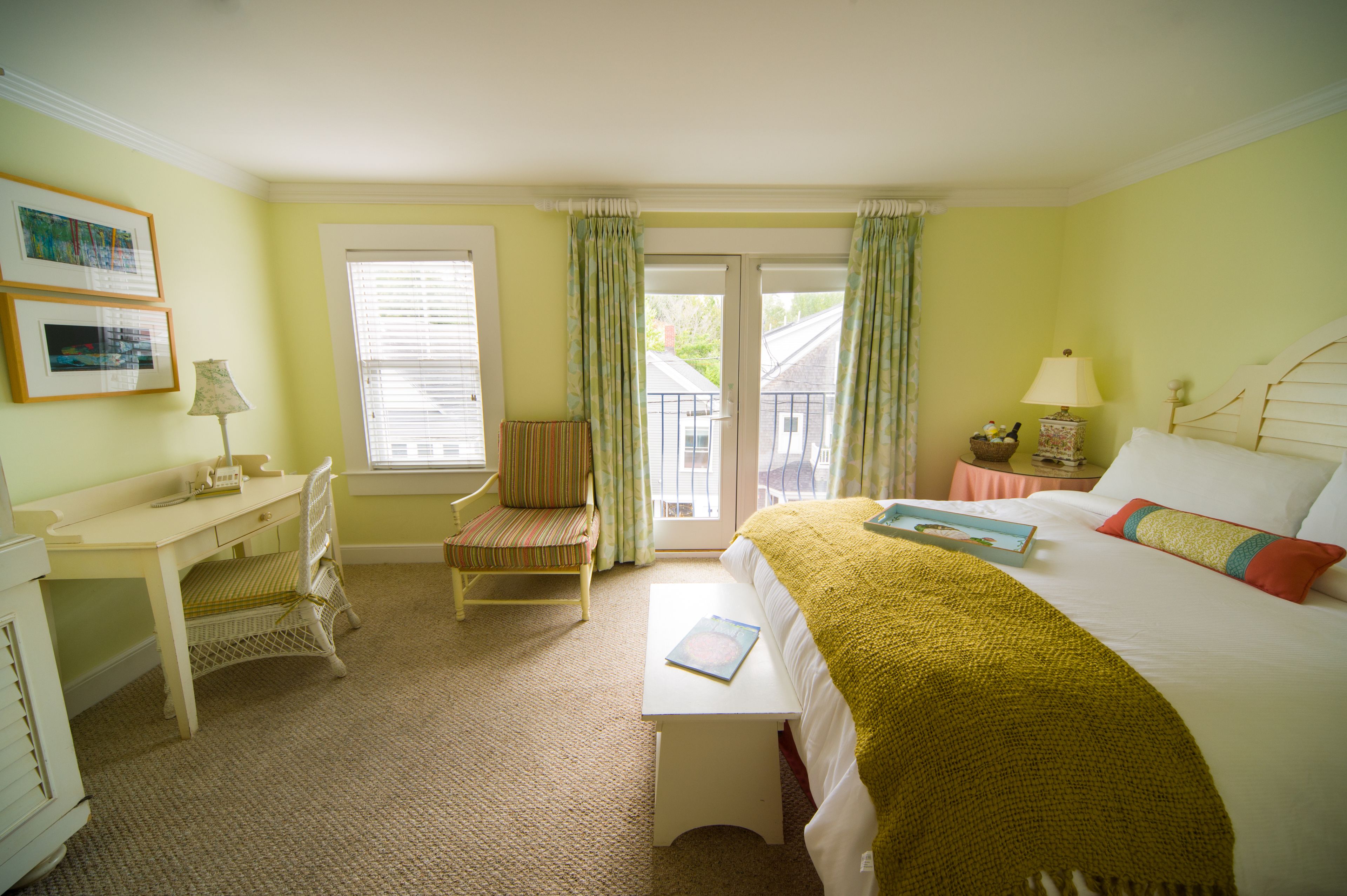 A hotel room with a bed, a desk, a chair, a small table, and a window with curtains.