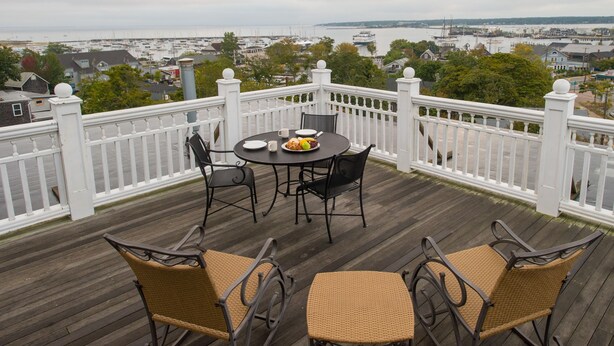 A wooden deck with a white railing, a round table with chairs, and a view of the marina and town in the background. - Mansion House Inn And Spa (Vineyard Haven)