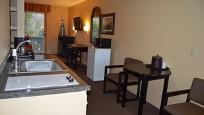 A compact kitchenette with a sink, stove, and microwave. There is a small refrigerator, a dining table with chairs, and a window with a view of greenery. - New World Inn (Barre)