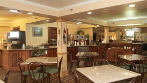 A hotel dining area with multiple tables and chairs, a kitchen area with appliances, and a bar. - New World Inn (Barre)