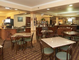 Un comedor de hotel con varias mesas y sillas, una zona de cocina con electrodomésticos y un bar.