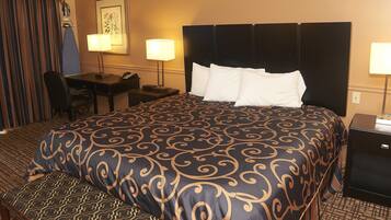A hotel room with a large bed, a desk, a chair, and a nightstand.