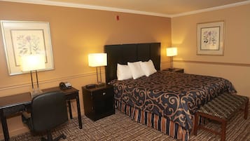 A hotel room with a bed, two bedside tables with lamps, a desk with a chair, and a bench.