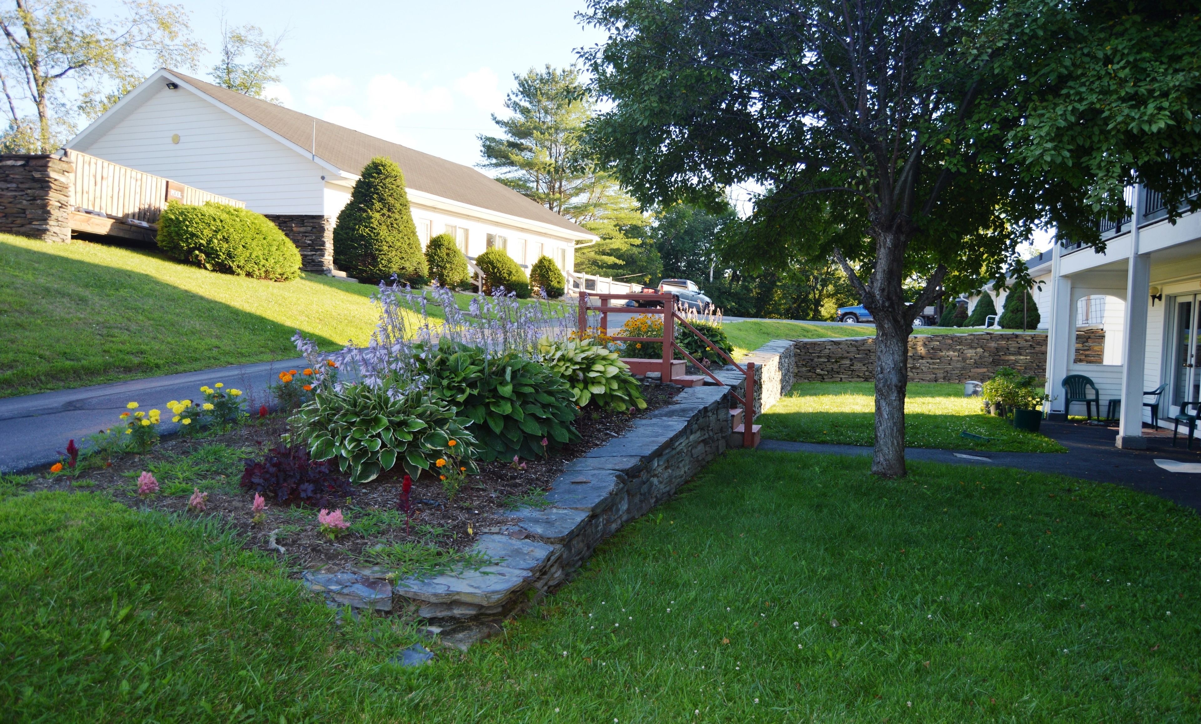 A residential area with a stone retaining wall, a well-maintained lawn, and a house with a porch.