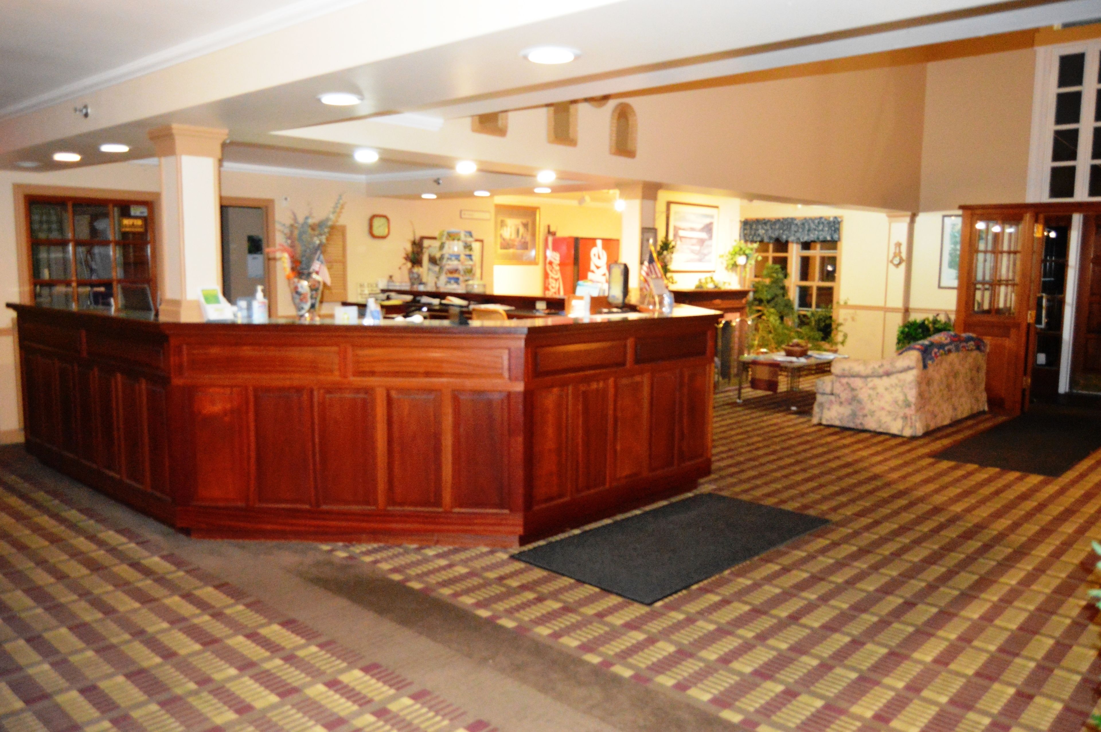 A reception area with a wooden counter, a reception desk, a seating area with a patterned carpet, and a door leading to another room.