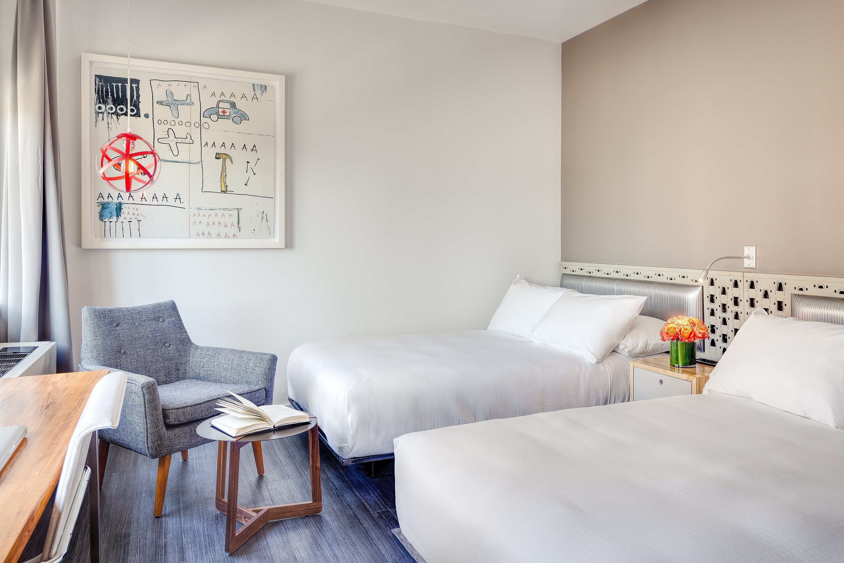 A hotel room with two beds, a desk, a chair, and a wall art piece.