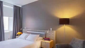 Una habitación de hotel con cama, mesita de noche, lámpara y sillón.