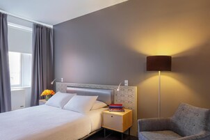 A hotel room with a bed, bedside table, lamp, and chair.