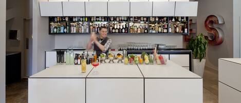 Un bar moderno con un cantinero, una variedad de botellas y vasos, y una planta grande en maceta.