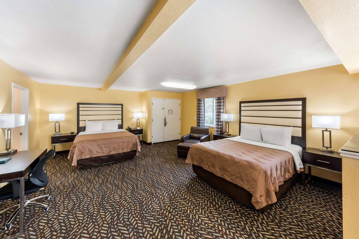 A hotel room with two beds, a desk, a chair, and a window with curtains.