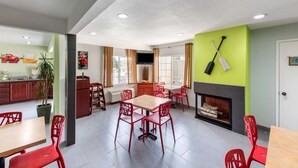 A modern dining area with red chairs and a wooden table, a kitchen with red cabinets, and a fireplace. - Quality Inn & Suites Capitola By the Sea (Capitola)