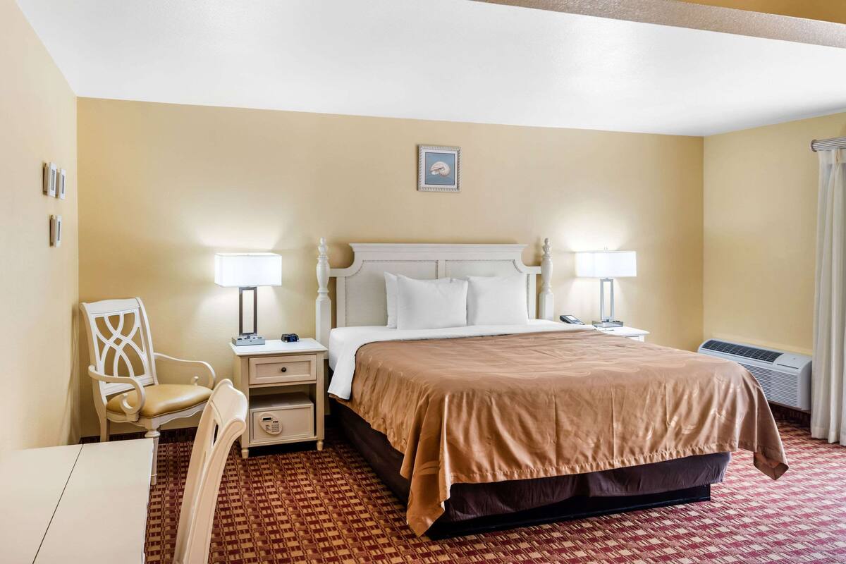 A hotel room with a bed, two bedside tables, a chair, a desk, and a patterned carpet.