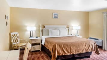 A hotel room with a bed, two bedside tables, a chair, a desk, and a patterned carpet.