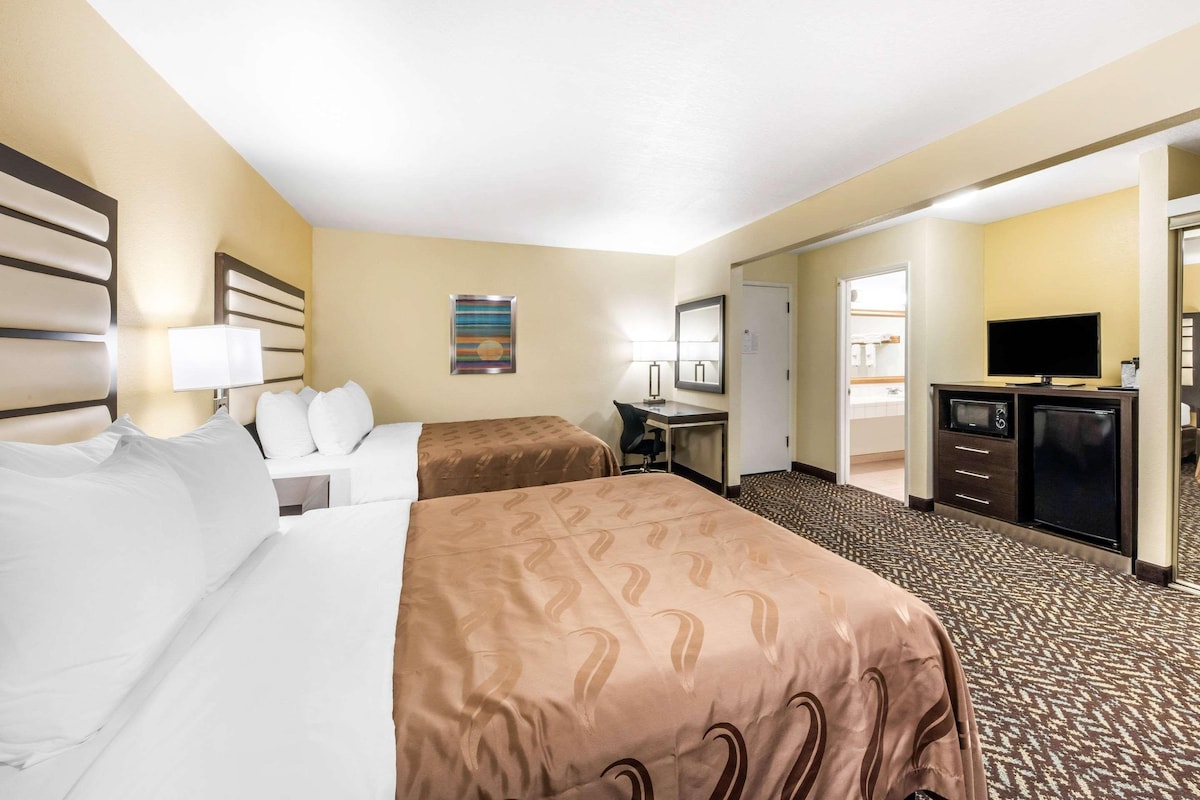 A hotel room with two beds, a desk, a TV, and a minibar.