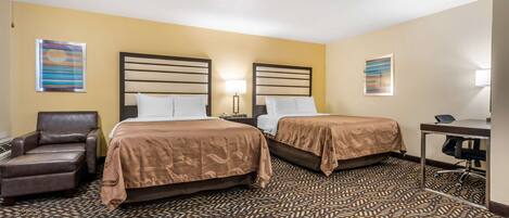 A hotel room with two beds, a desk, a chair, and a patterned carpet.