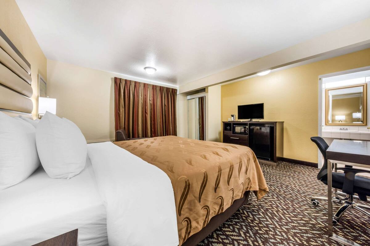 A hotel room with a bed, a desk, a television, and a mirror.