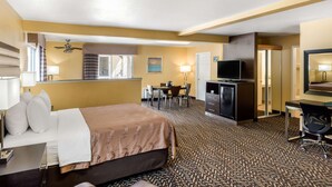 A hotel room with a bed, desk, chair, TV, and a small kitchenette. - Quality Inn & Suites Capitola By the Sea (Capitola)