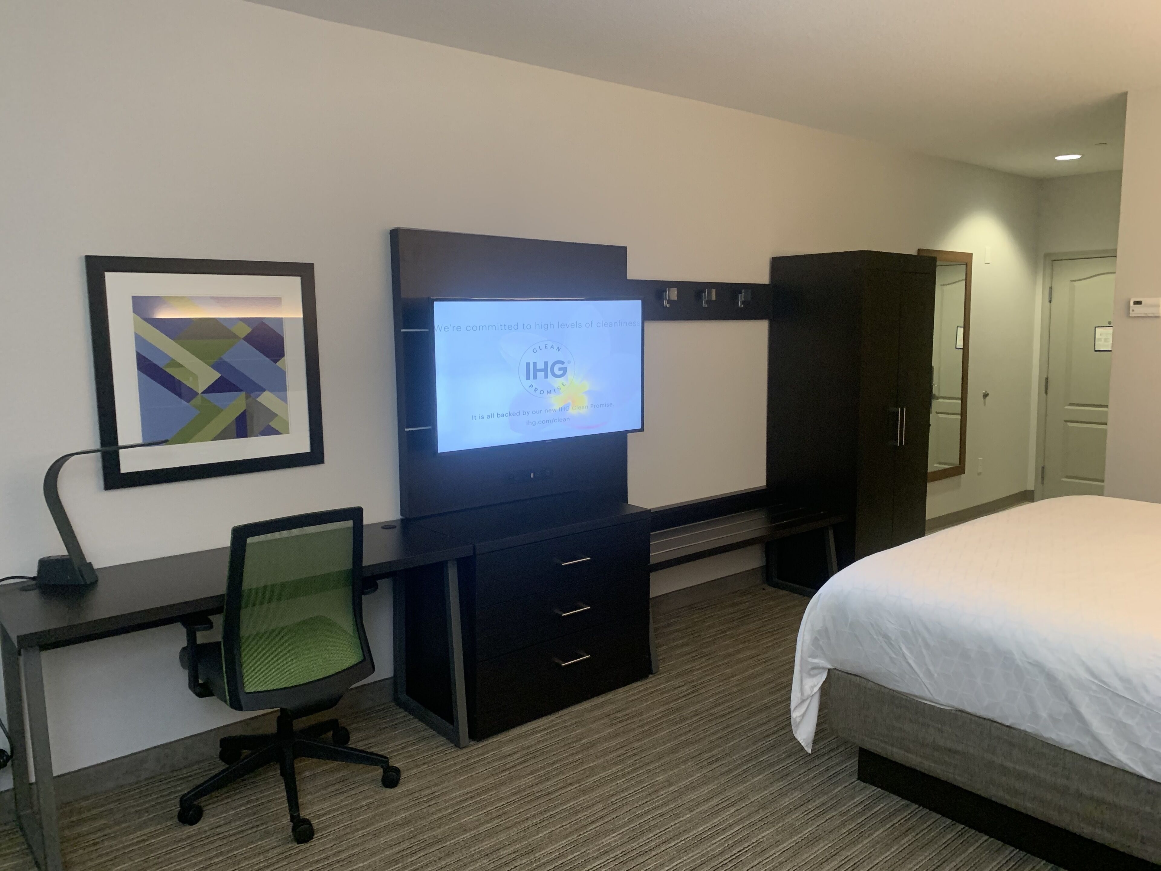 Una habitación de hotel con cama, escritorio, silla, televisor y armario.