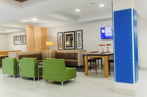 Un área de descanso moderna con un sofá modular, sillones verdes, un separador de madera y un televisor montado en la pared.
