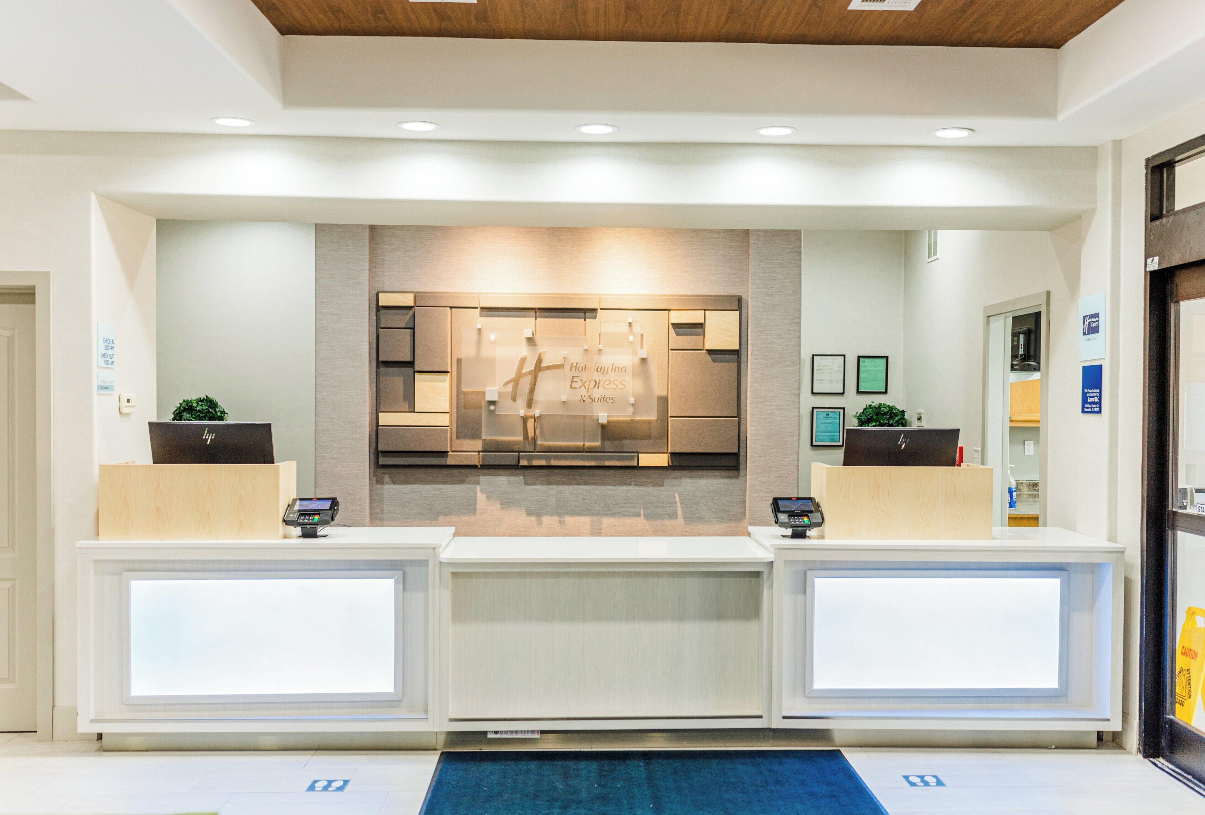 A reception area with a modern design, featuring a reception desk, a wall-mounted display, and a blue carpet.
