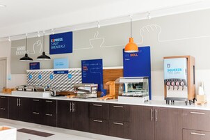 Una barra de desayuno moderna con diversas opciones de alimentos, incluyendo una máquina de café y un dispensador de jugos.