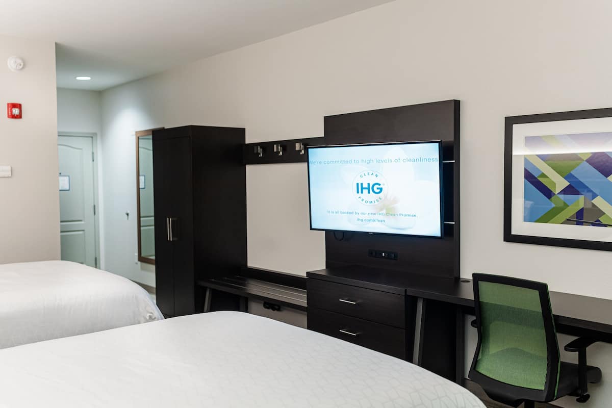 A hotel room with two beds, a desk with a computer, a TV displaying a message, and a framed picture on the wall.