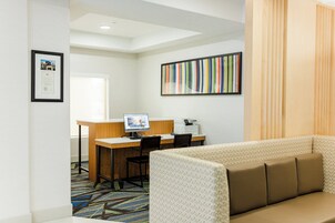 A hotel room with a desk, a computer, a printer, a sofa, and a colorful striped artwork on the wall.
