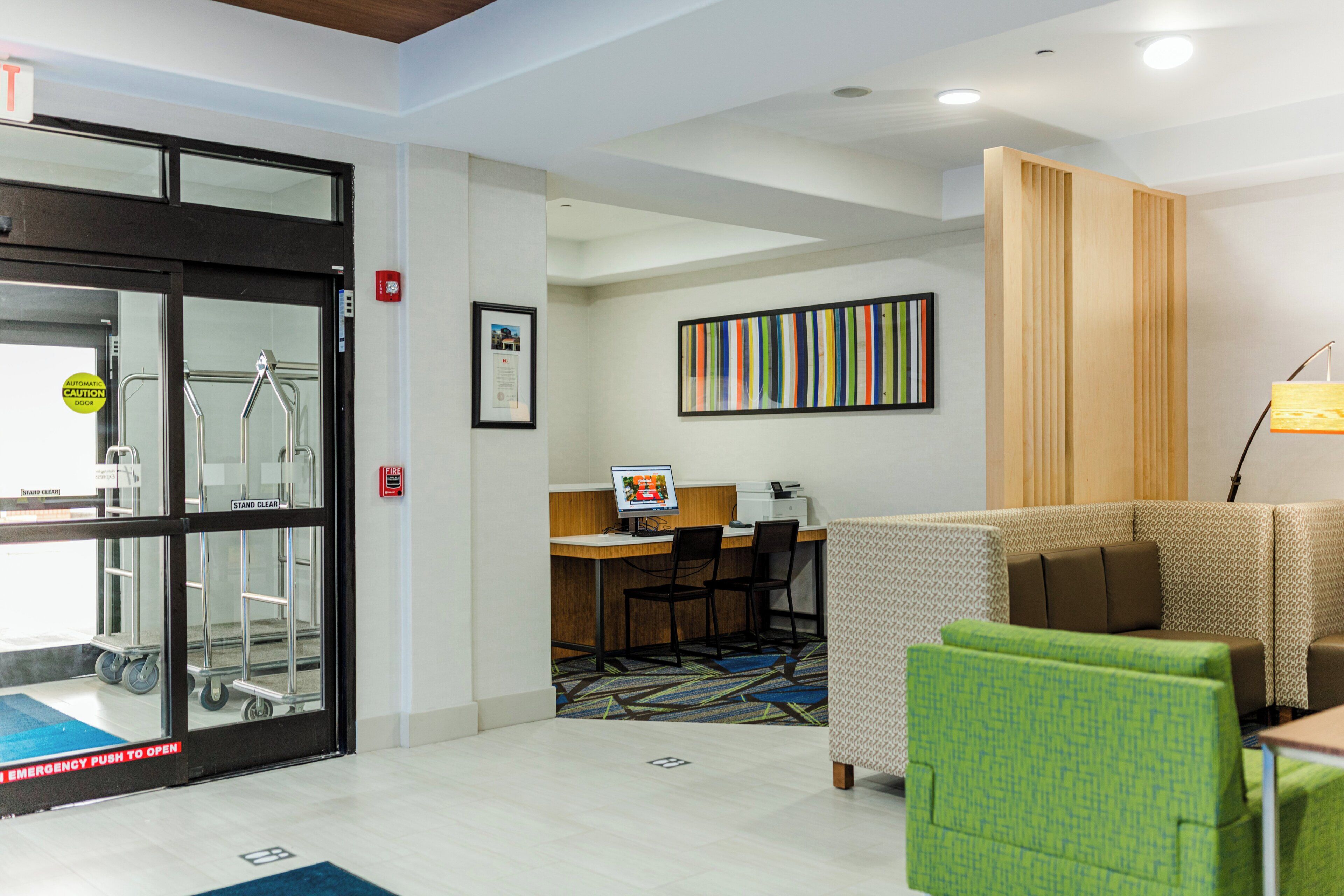 A hotel lobby with a reception desk, a fire alarm, a framed certificate, and a colorful striped artwork.