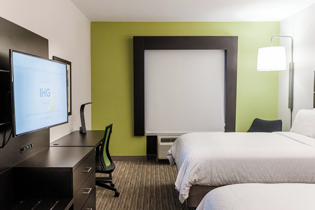 A hotel room with a bed, a desk with a computer, a chair, and a large window.
