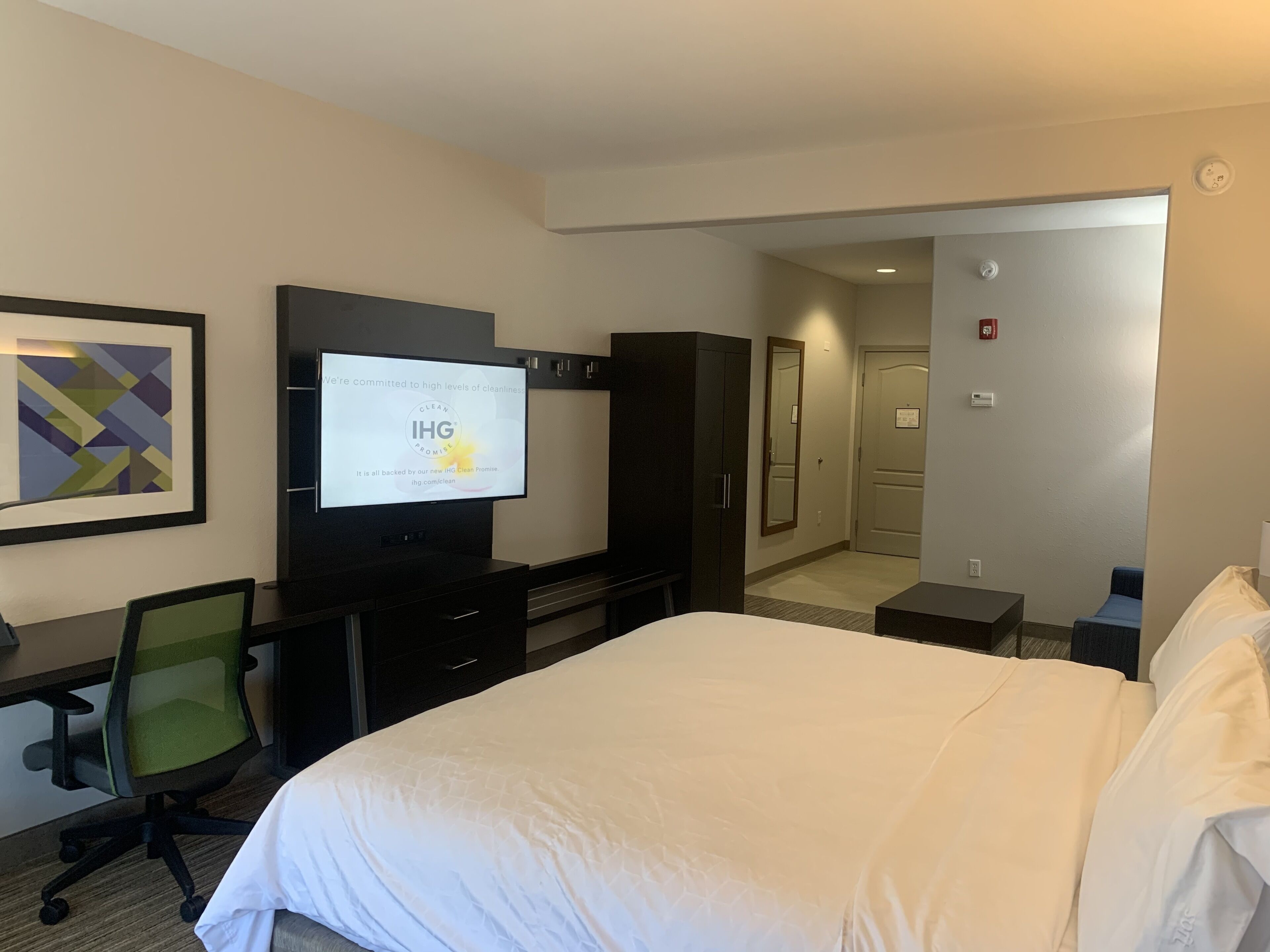 A hotel room with a bed, a desk, a chair, a television, and a door leading to another room.