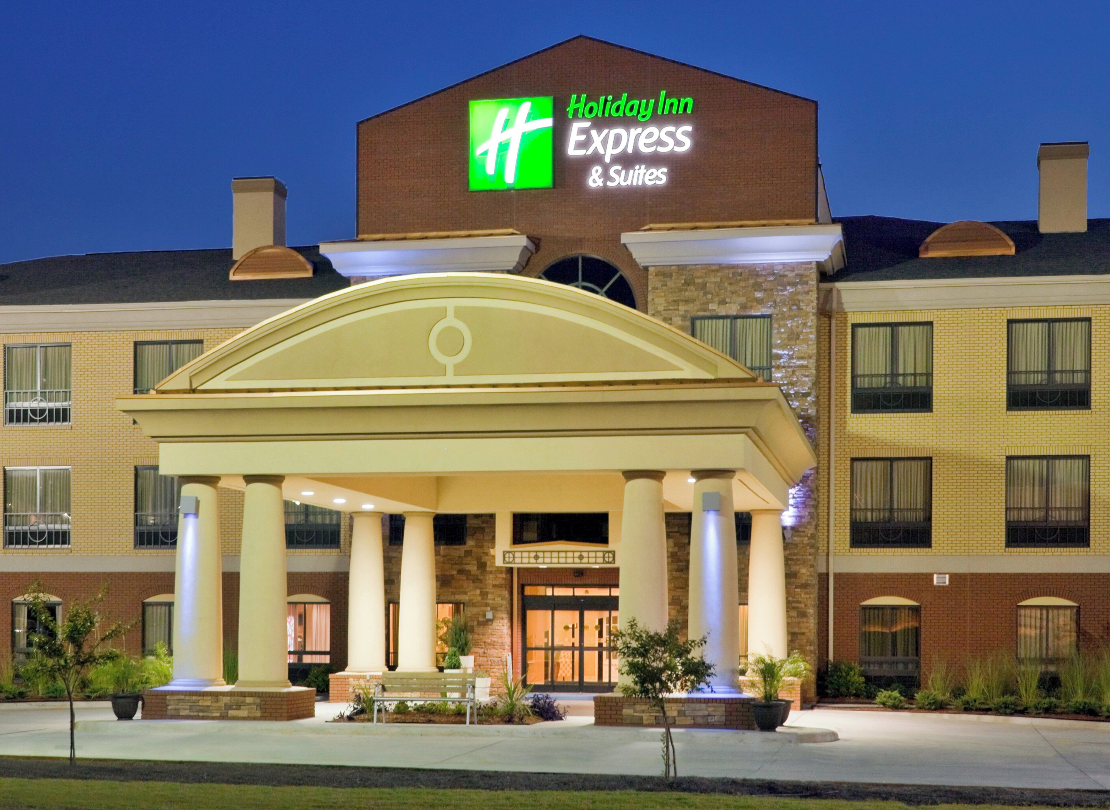 A Holiday Inn Express & Suites hotel with a prominent entrance, columns, and a well-lit facade.