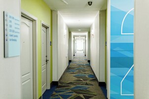 A hotel hallway with doors on both sides, a patterned carpet, and a blue geometric design on the wall.