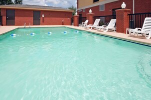 A swimming pool with clear water, surrounded by white lounge chairs and a brick building.