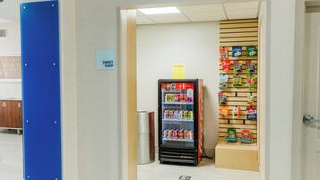 Een automaat gevuld met snacks en drankjes, een prullenbak en een bordje dat een snoepwinkel aangeeft.