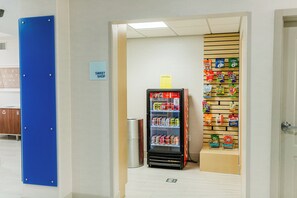 Un distributeur automatique rempli d’en-cas et de boissons, une poubelle et un panneau indiquant l’emplacement d’une confiserie.
