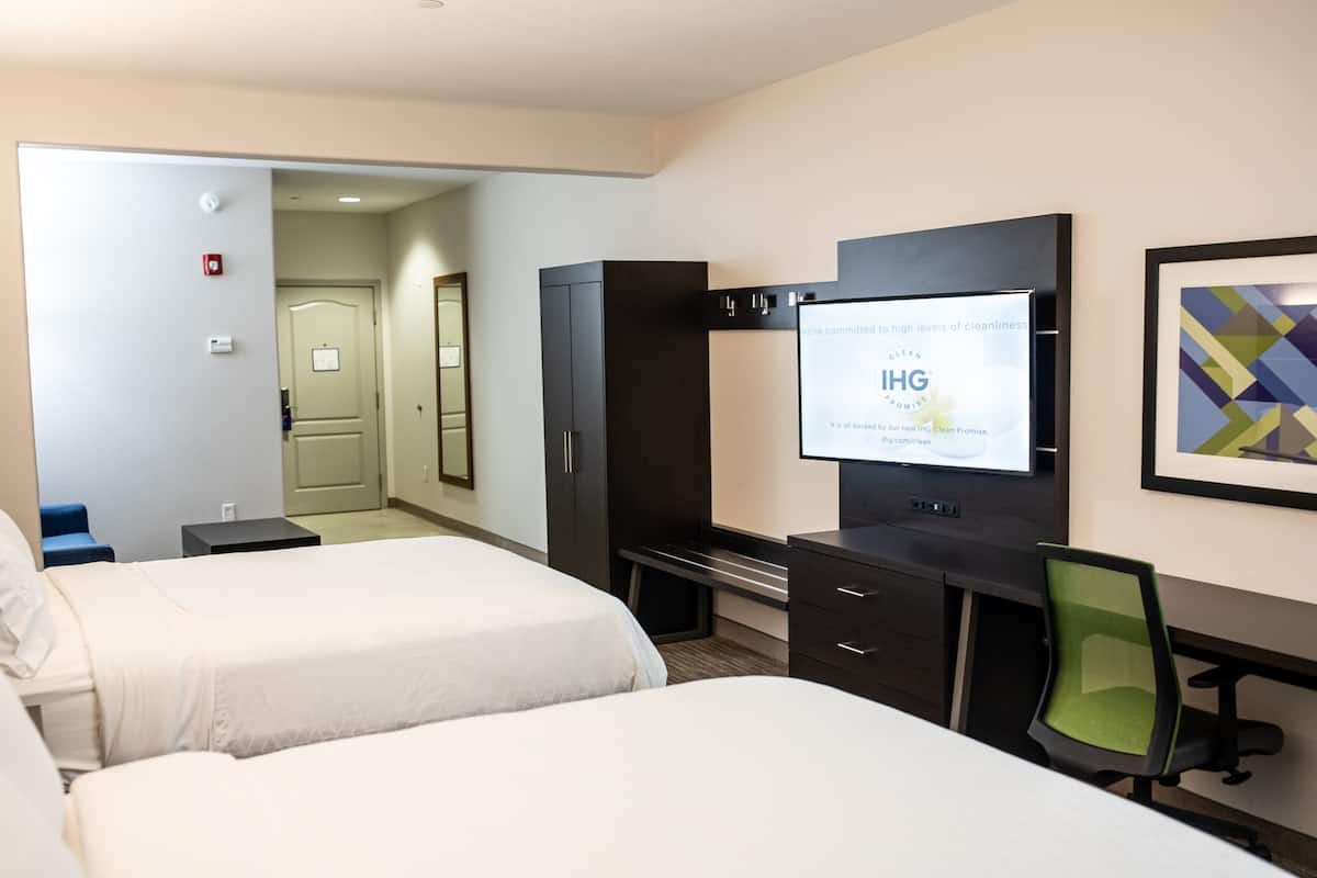 A hotel room with two beds, a desk, a chair, a TV, and a framed picture on the wall.