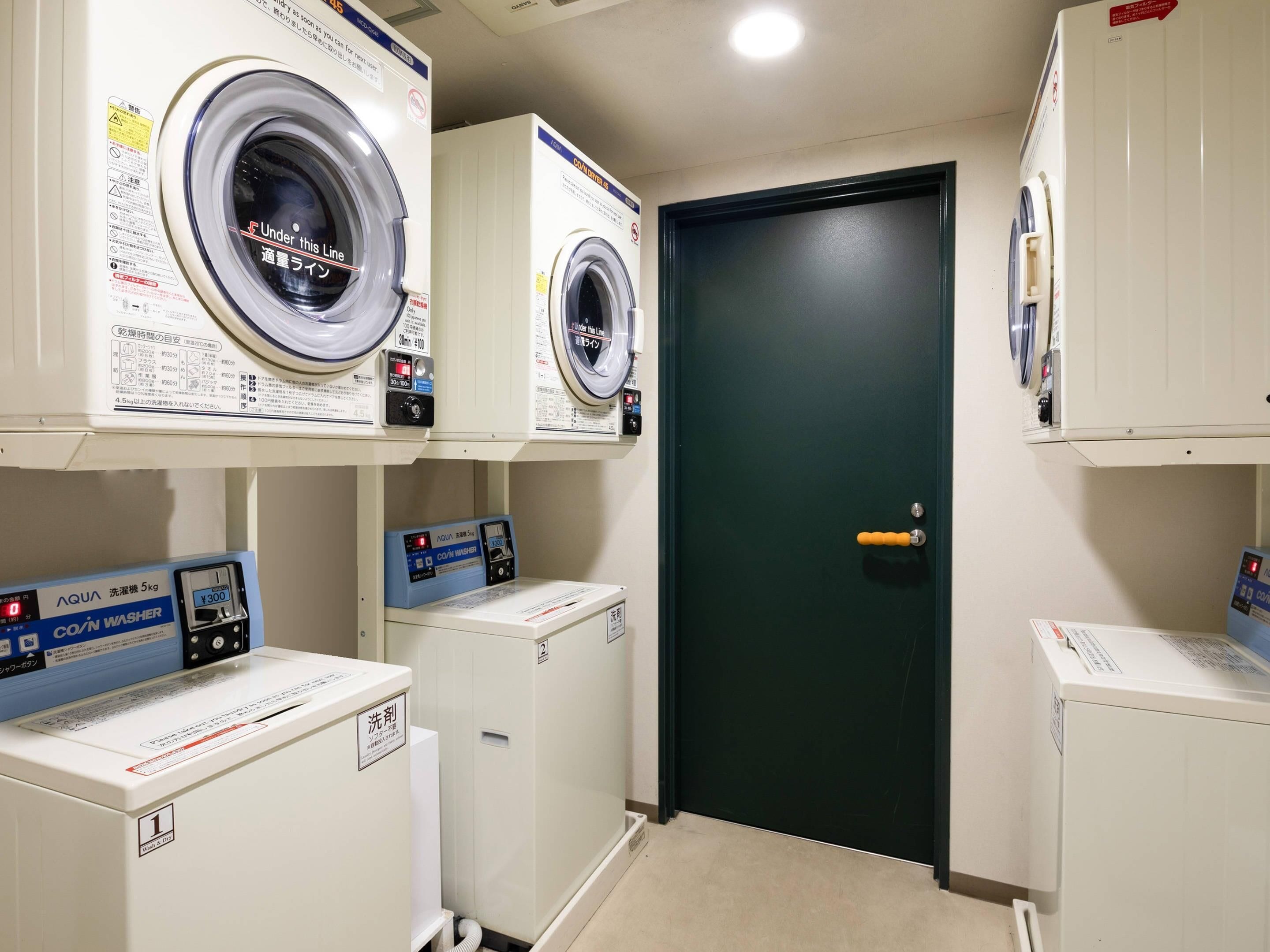 A laundry room with multiple washing machines and dryers, a green door, and a white tiled floor.