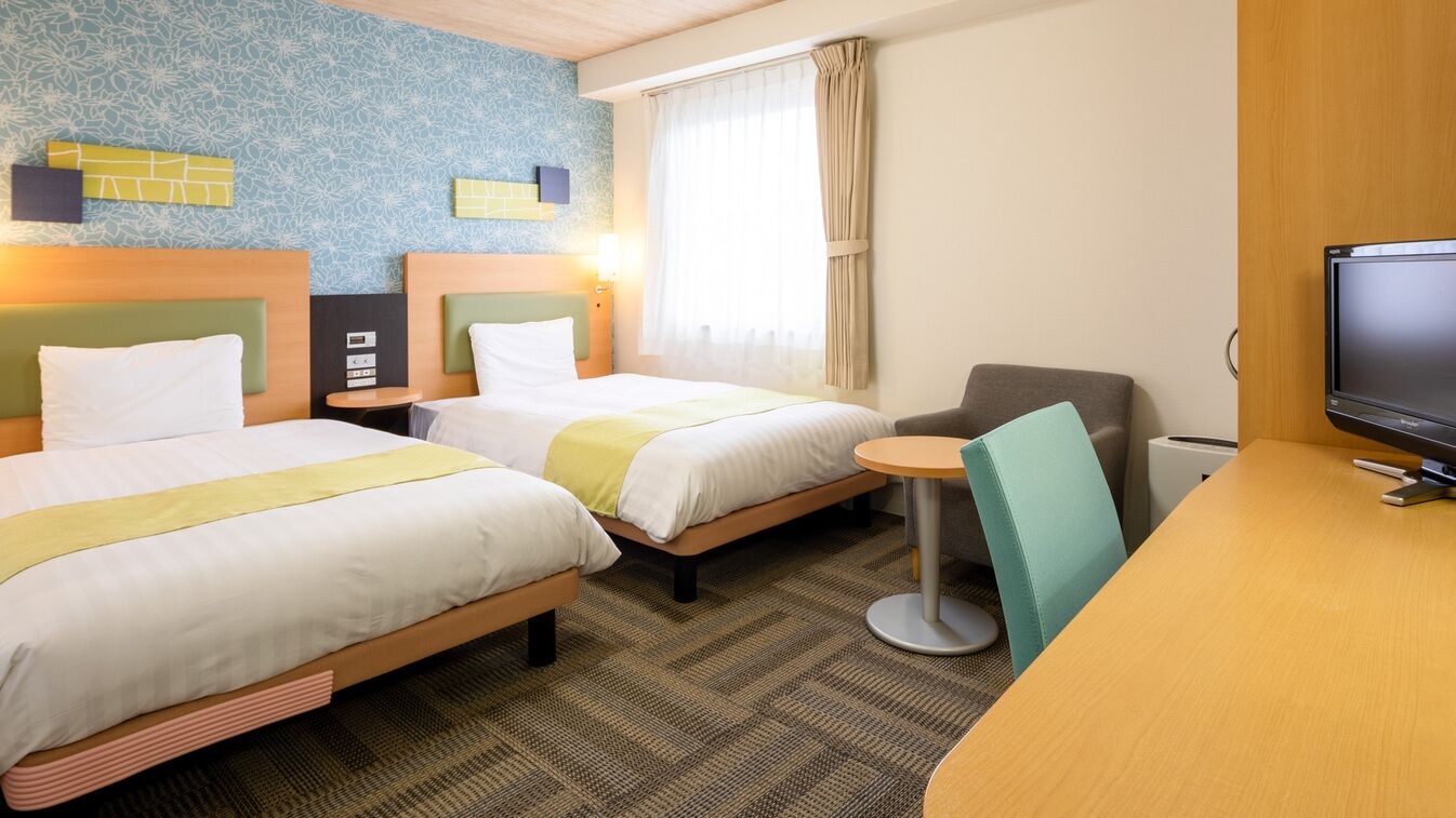 A hotel room with two beds, a desk, a television, and a window with curtains.