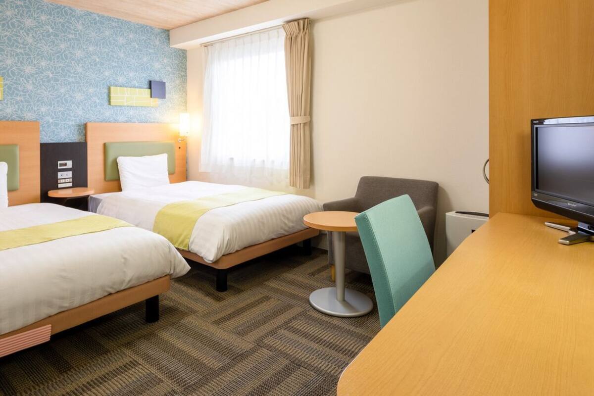 A hotel room with two beds, a desk, a television, and a window with curtains.
