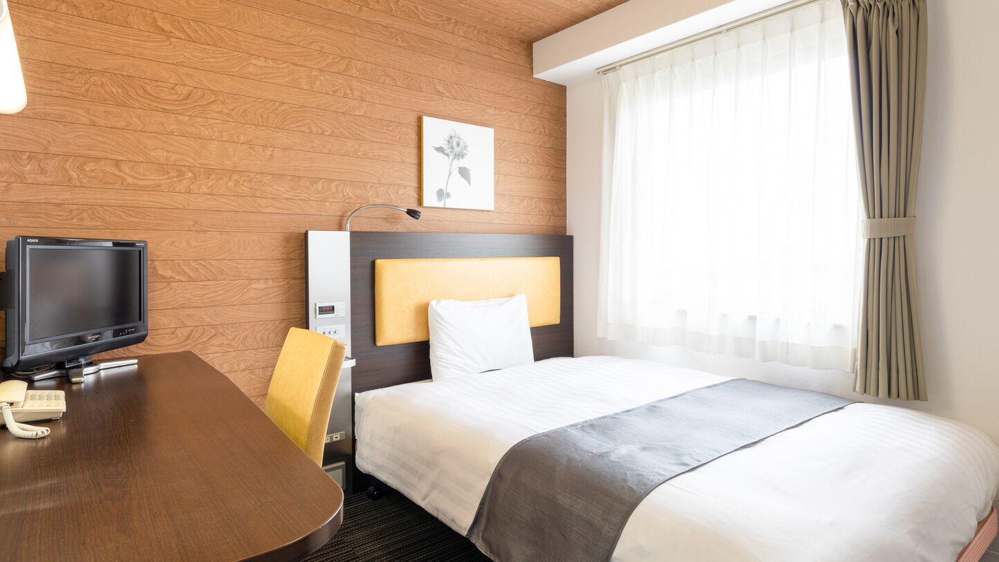 A hotel room with a wooden wall, a bed with white bedding, a desk with a television, and a telephone.