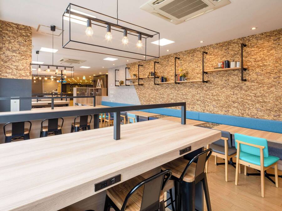 A modern cafe with wooden tables and chairs, a counter, and a wall with shelves.