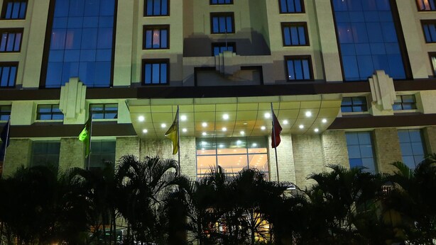 Un hotel de varios pisos con un diseño moderno, que presenta una entrada destacada con fachada de vidrio y una serie de ventanas en cada planta.