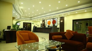 Vestíbulo de hotel con mostrador de recepción, asientos color naranja y una mesa de centro de cristal.