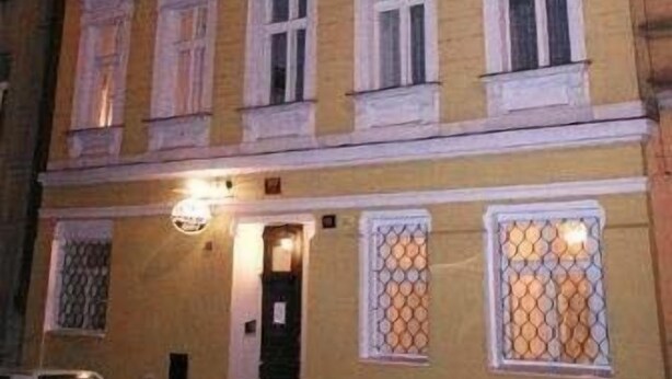A multi-story building with a yellow facade, white window frames, and a door with a metal grille. - Pension Prague City (Prague)