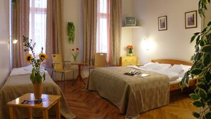 A hotel room with two beds, a wooden floor, a small table with a vase of flowers, and a television on a stand. - Pension Prague City (Prague)