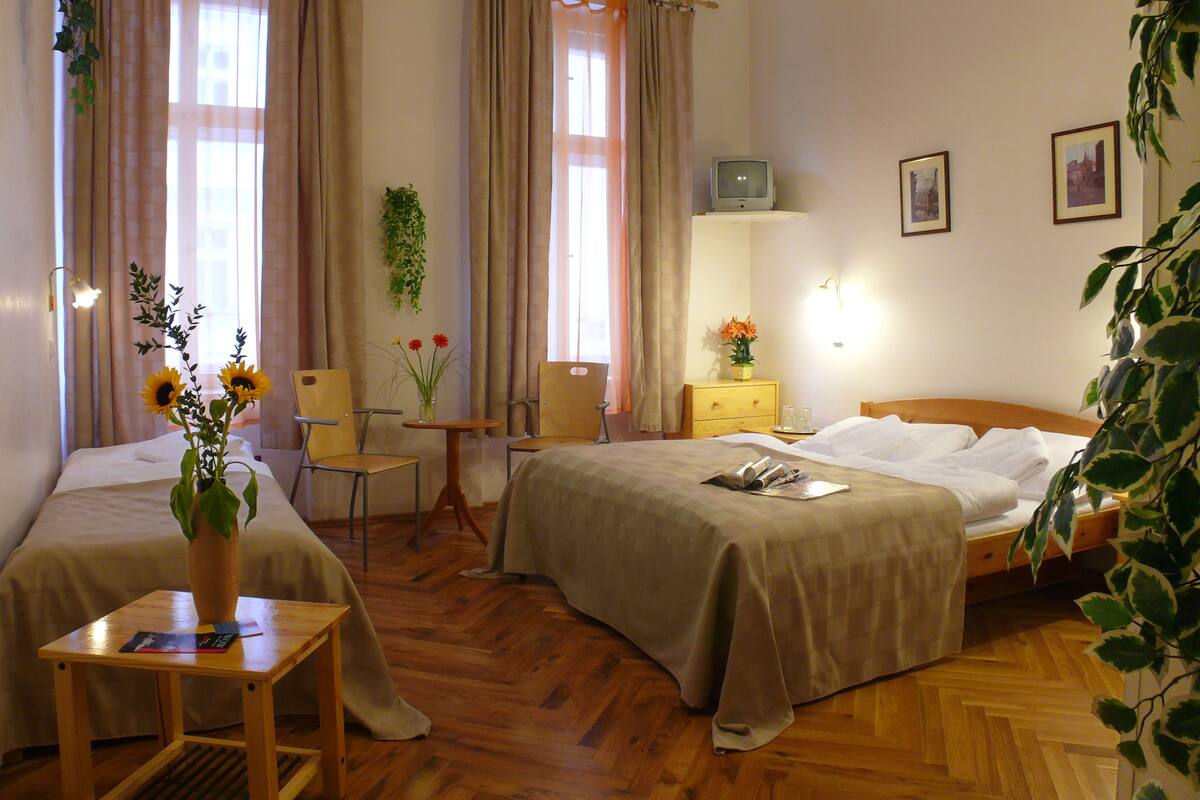 A hotel room with two beds, a wooden floor, a small table with a vase of flowers, and a television on a stand.