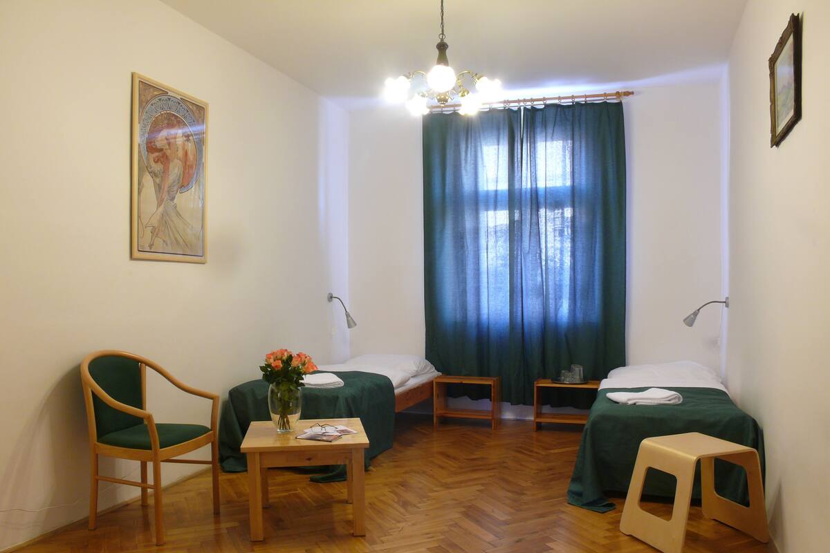 A room with two beds, a chair, a small table with a vase of flowers, and a painting on the wall.