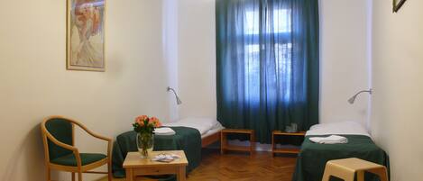 Quarto com duas camas, uma cadeira, uma mesinha com um vaso de flores e um quadro na parede.