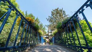Un puente de madera con barandillas de metal ornamentadas, rodeado de abundante follaje y árboles.